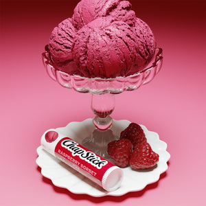 Raspberry sorbet lip balm tube on white plate with fresh raspberries